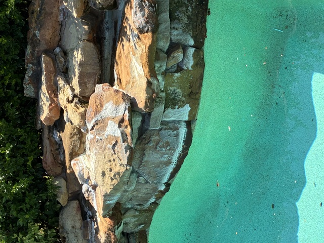 Before: A natural stone retaining wall rises above bright turquoise pool water.